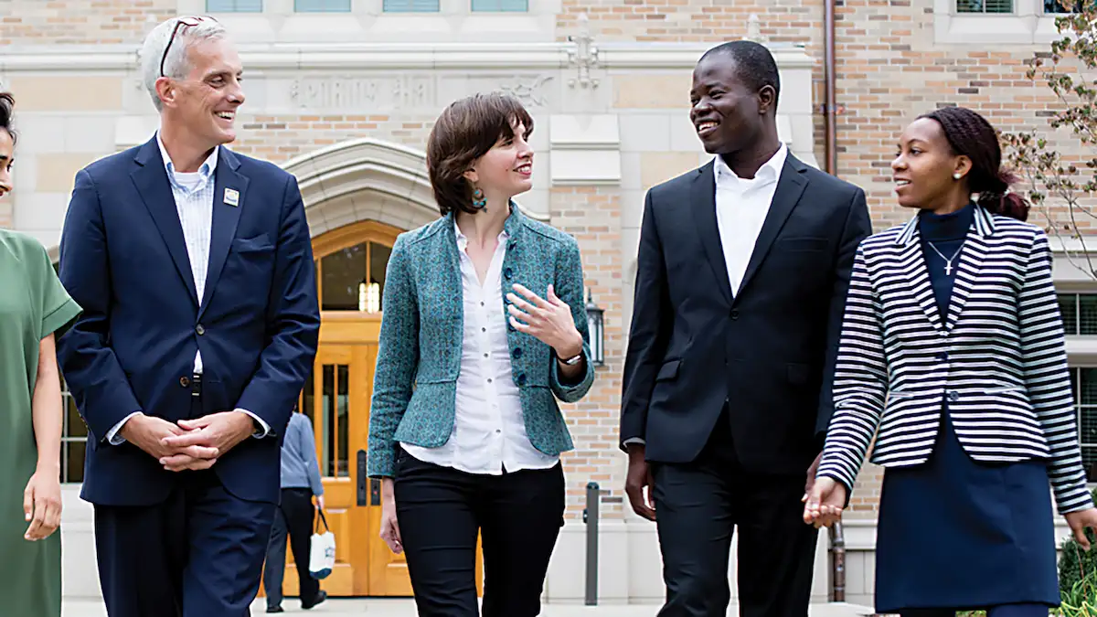 Four people walk and talk in front of a brick building on the University of Notre Dame campus.