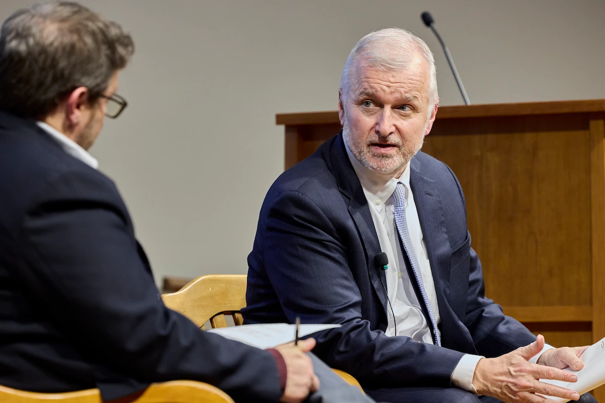 Former diplomat Thomas Christensen, a gray-haired man with a beard, wearing a dark blue suit and light blue tie, speaks intently while gesturing with his hands.