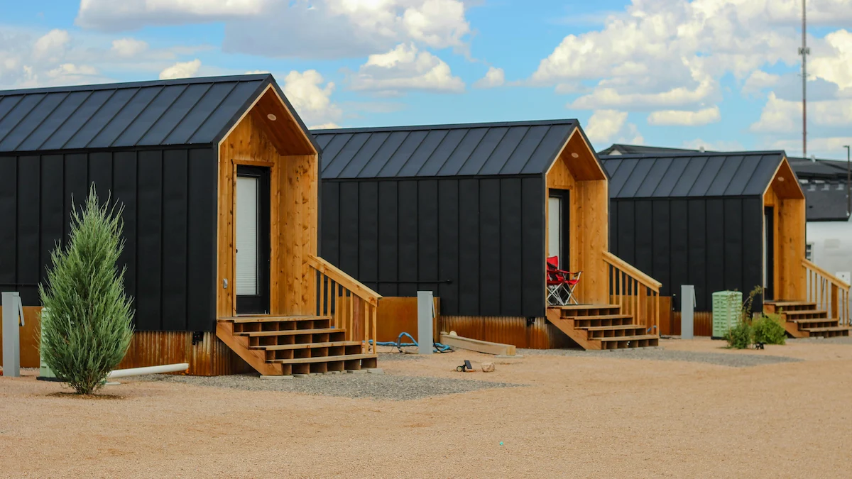 A row of modern, black metal-clad tiny homes with natural wood entryways and porches, illustrating innovative building technologies for affordable housing.