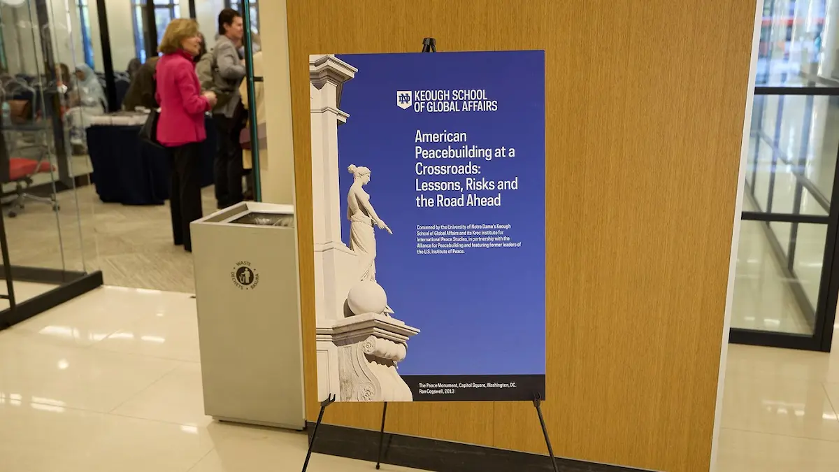 Blue Keough School poster with white Peace Monument statue. Title: American Peacebuilding at a Crossroads.