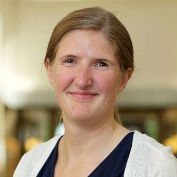 Woman with light brown hair in a dark blue top and white cardigan, smiling gently indoors.