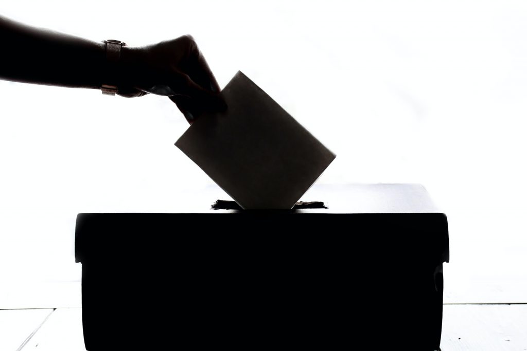 Black and white photo of hand dropping voting ballot into a box