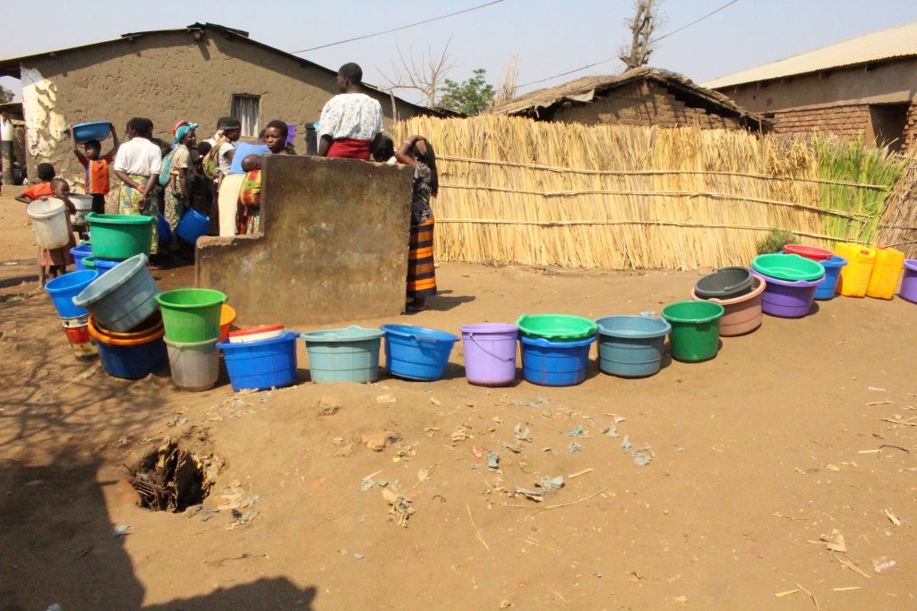 a line of colorful plastic water buckets outside a well in Malawi