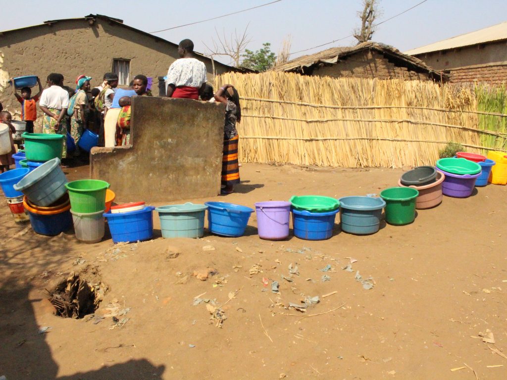 a line of colorful plastic water buckets outside a well in Malawi