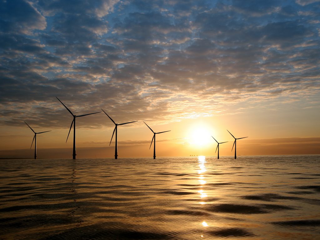 Wind turbines on the ocean with the sun in the backgound