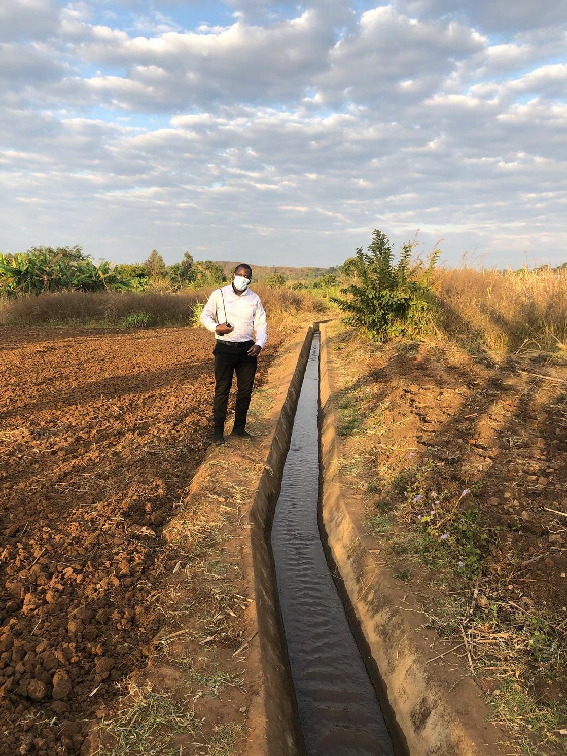a man wearing a mask stands next to an irrigation ditch 