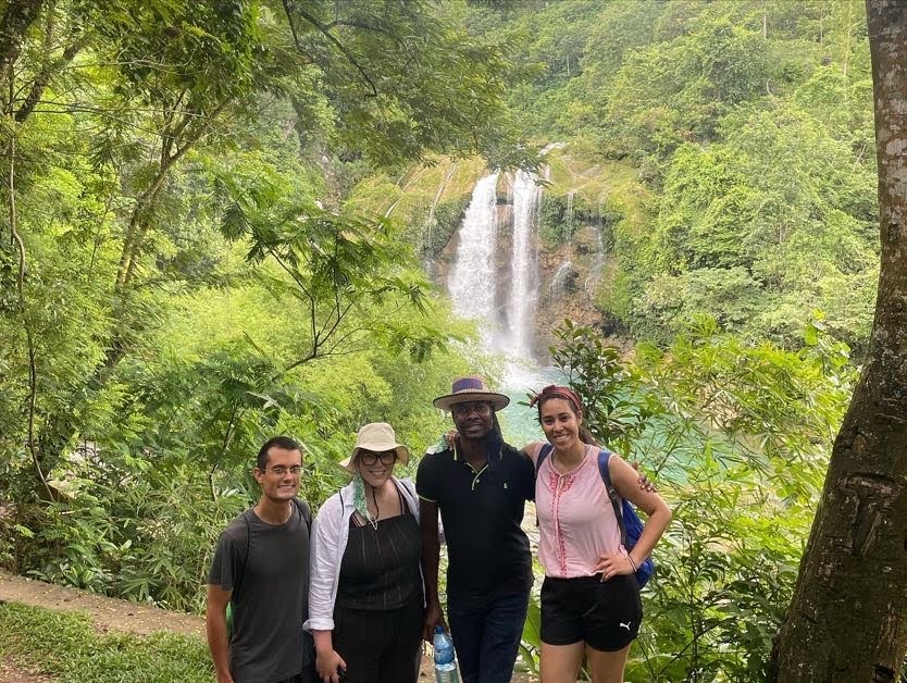 Four students standing in front of lush greenery and a waterfall.