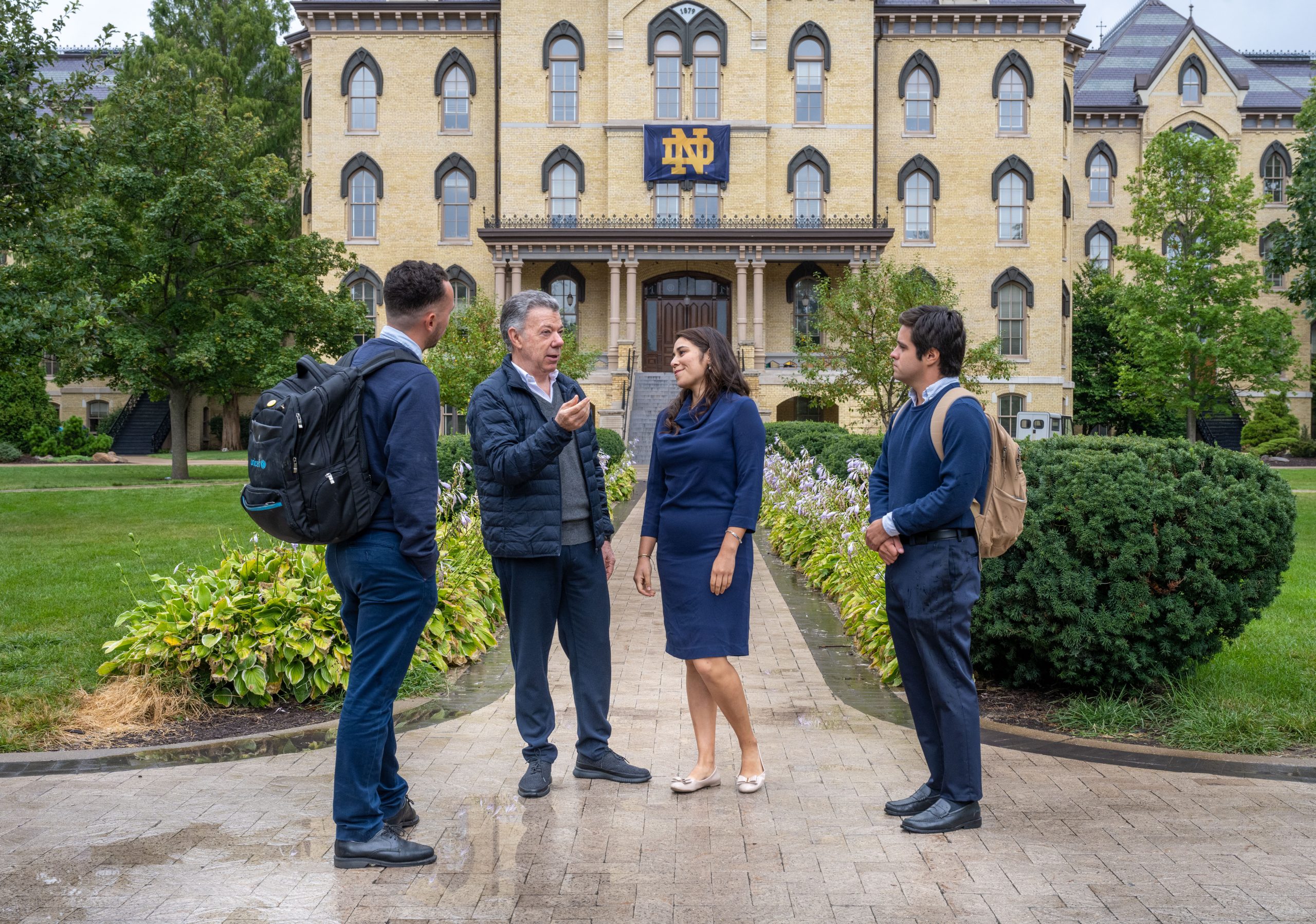 President Santos and three students talk in front of Notre Dame's Main Building.